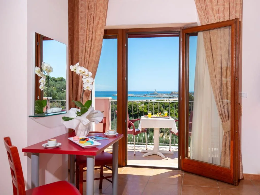 Scrivania con orchidea e porta finestra aperta su terrazza con vista mare e faro