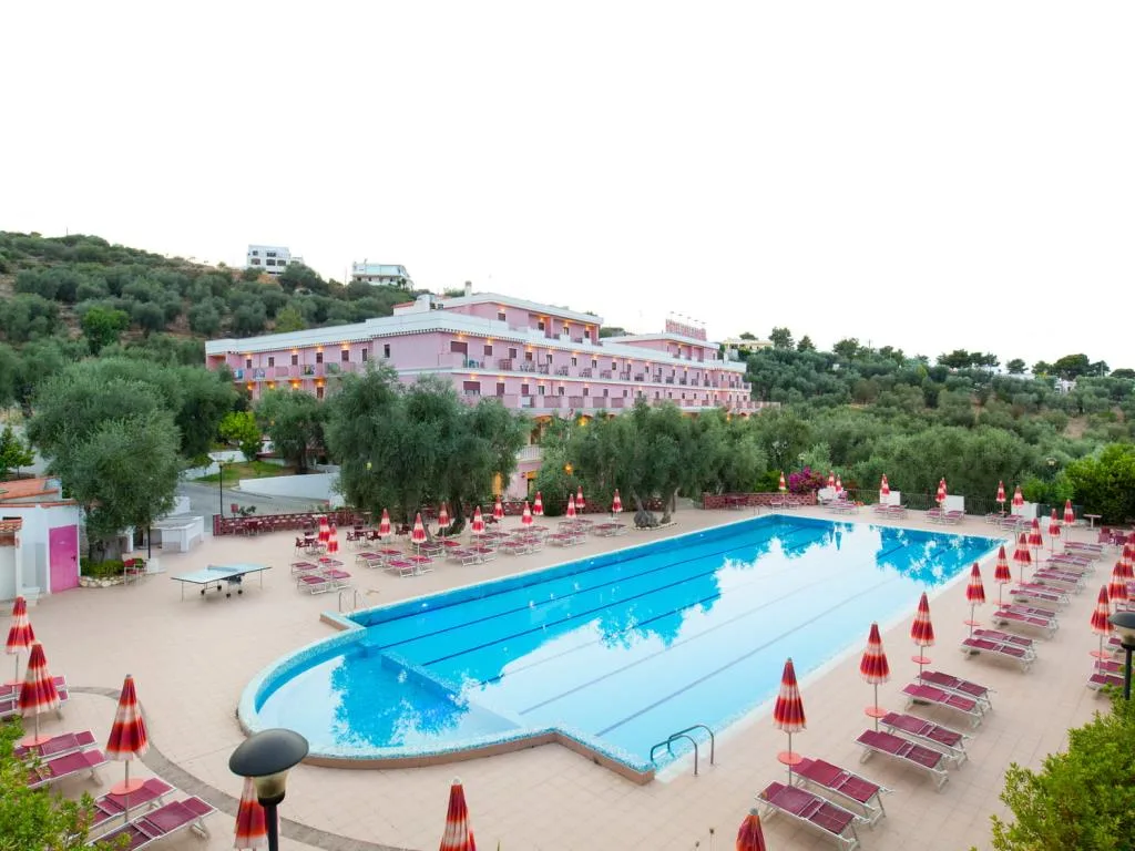 Hotel rosa con grande piscina circondata da lettini e ombrelloni al tramonto