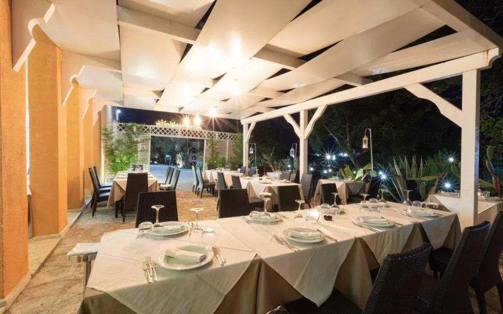 Ristorante esterno serale con tavoli apparecchiati sotto pergolato bianco