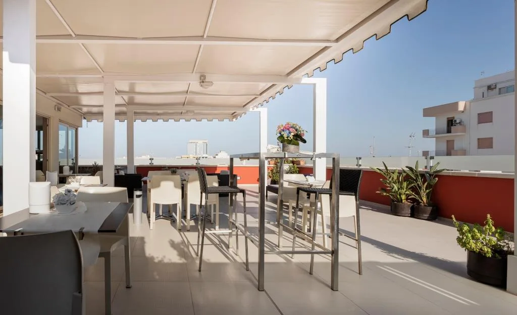 Terrazza solarium con tavoli alti, sedie e vista panoramica sotto pergola bianca
