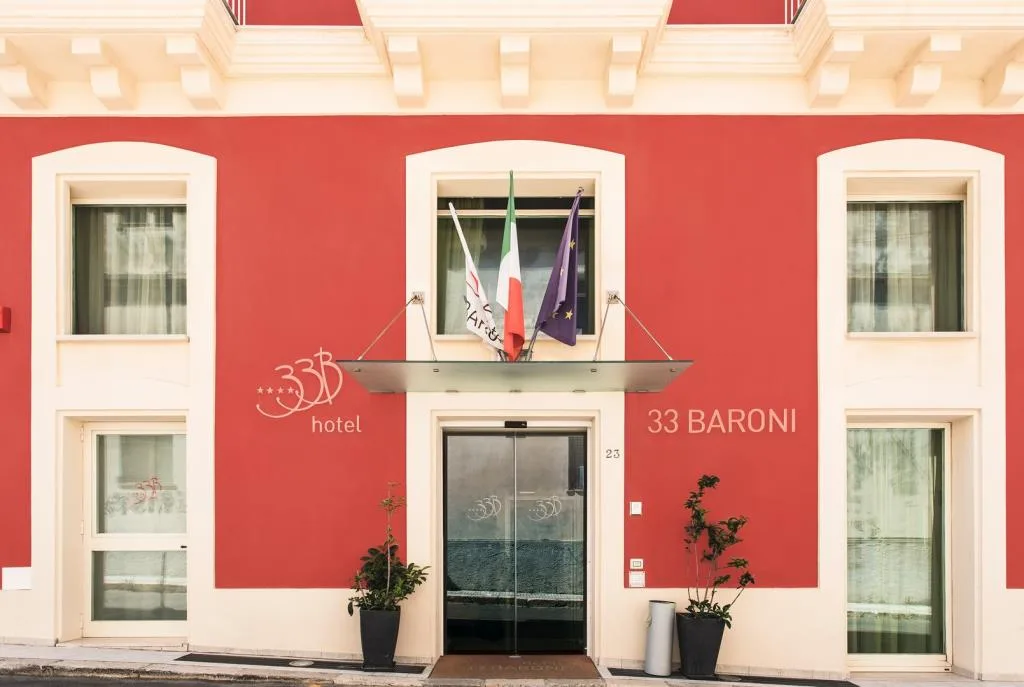 Facciata rossa dell'Hotel 33 Baroni con bandiere e ingresso vetrato