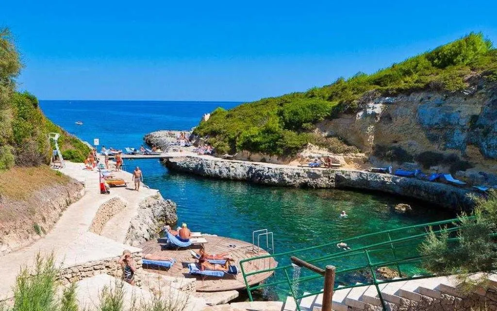 Insenatura rocciosa con acque limpide, solarium e bagnanti sulla costa