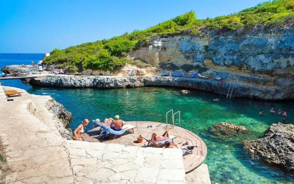 Cala rocciosa con acque verdi smeraldo e persone in relax su piattaforma in legno