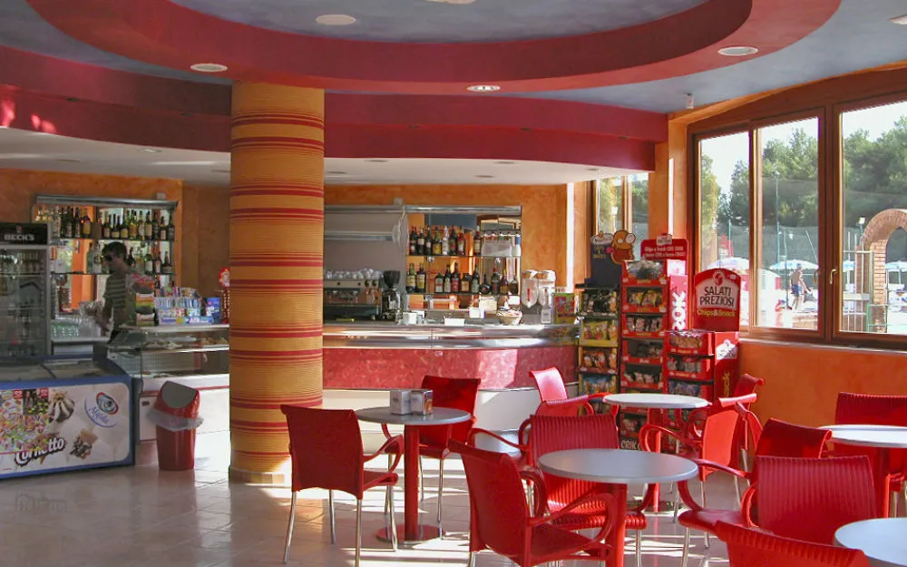 Bar interno con bancone, tavolini e sedie rosse e snack in vendita