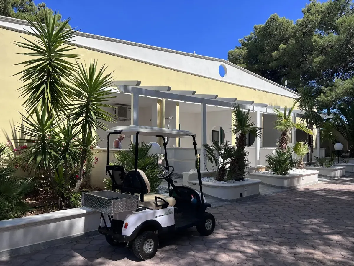 Esterno di edificio giallo del resort con pergolato bianco, palme e golf cart parcheggiato