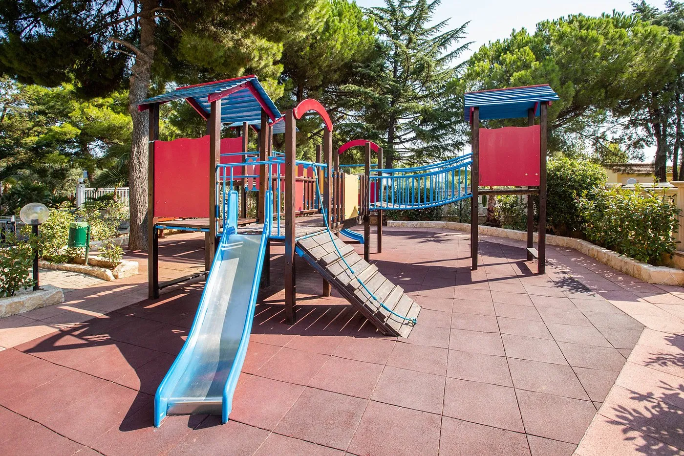 Parco giochi per bambini con scivolo, ponte sospeso e struttura in legno tra alberi