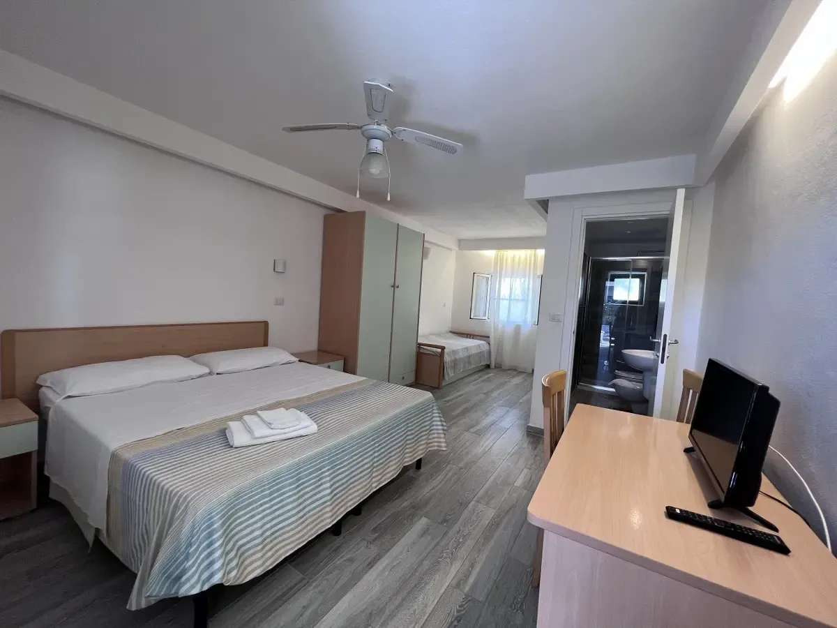 Camera con letto matrimoniale e letto singolo, ventilatore a soffitto, scrivania con TV e bagno