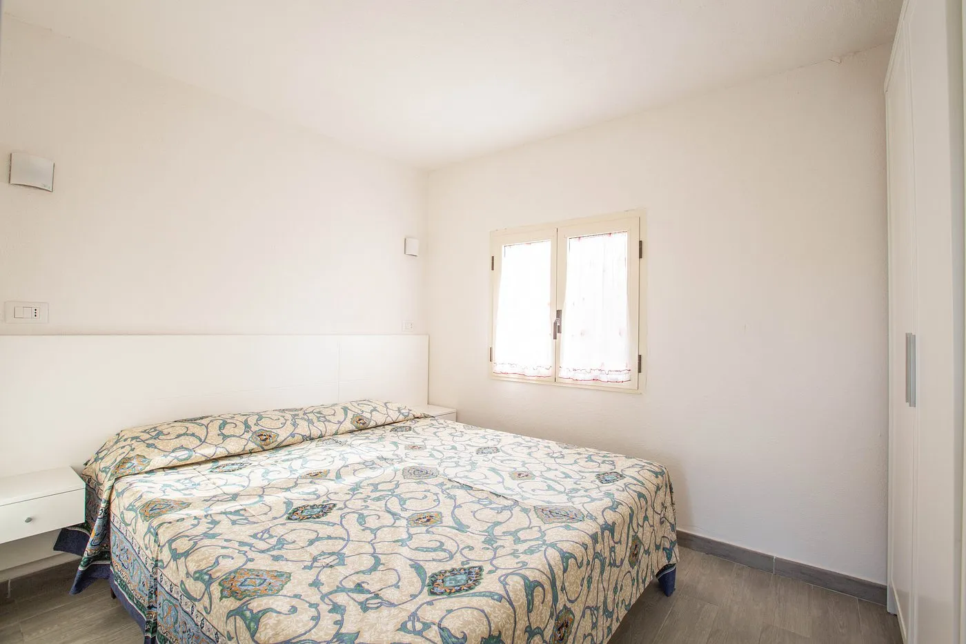 Camera da letto con letto matrimoniale, copriletto floreale, armadio bianco e finestra