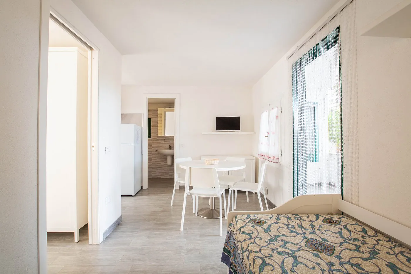 Monolocale luminoso con angolo cottura, tavolo bianco, TV e letto, pavimento in laminato