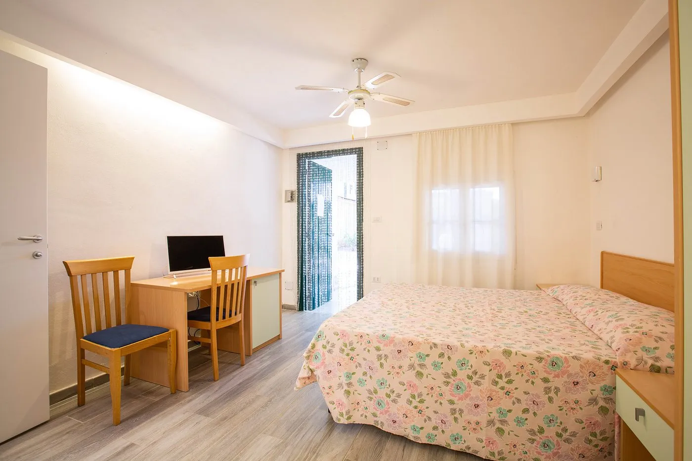 Camera con letto matrimoniale, scrivania con sedie e TV, accesso al giardino esterno