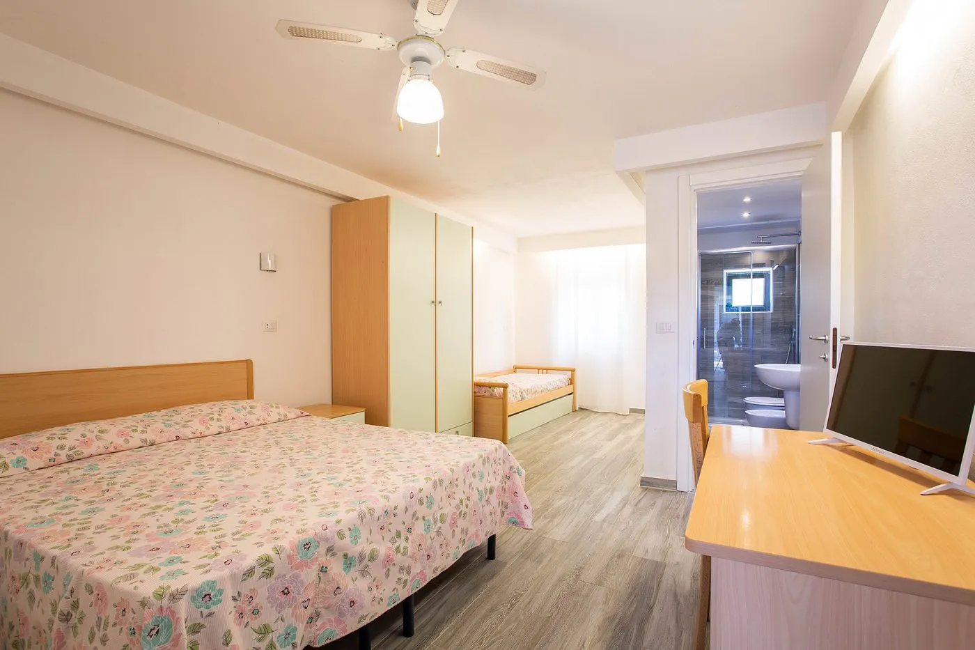 Camera con letto matrimoniale e singolo, copriletto floreale, ventilatore a soffitto e bagno
