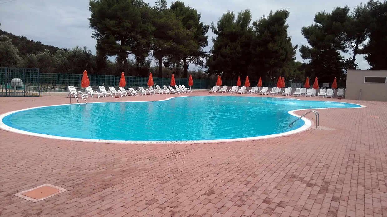 Piscina curvilinea con lettini bianchi e ombrelloni chiusi in giornata nuvolosa