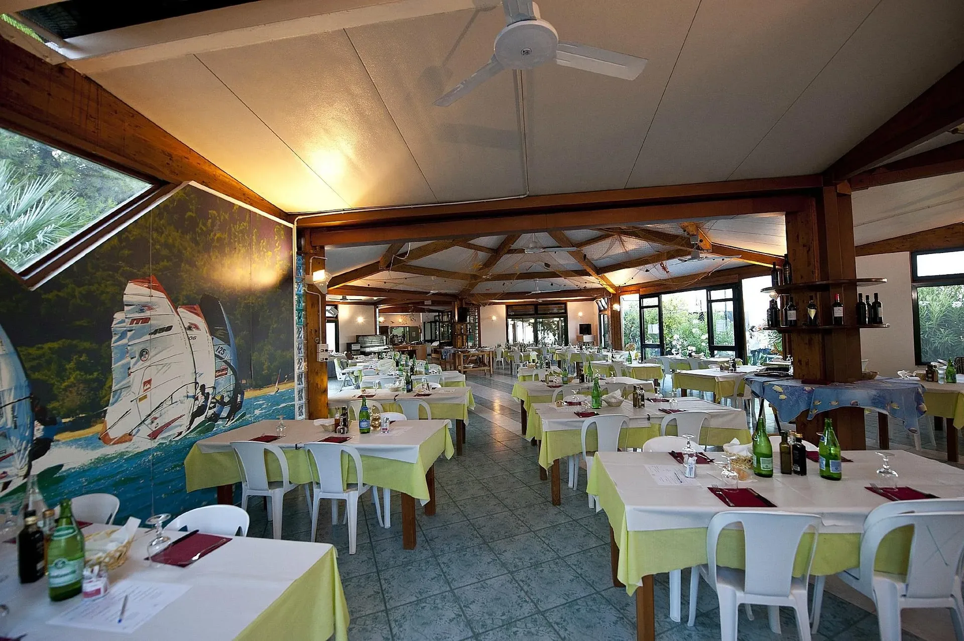 Interno del ristorante con travi in legno, murale di windsurf e tavoli apparecchiati