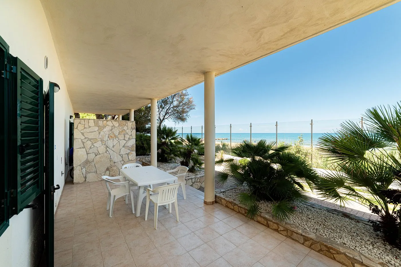 Veranda con tavolo e sedie bianche e vista sul mare tra le palme