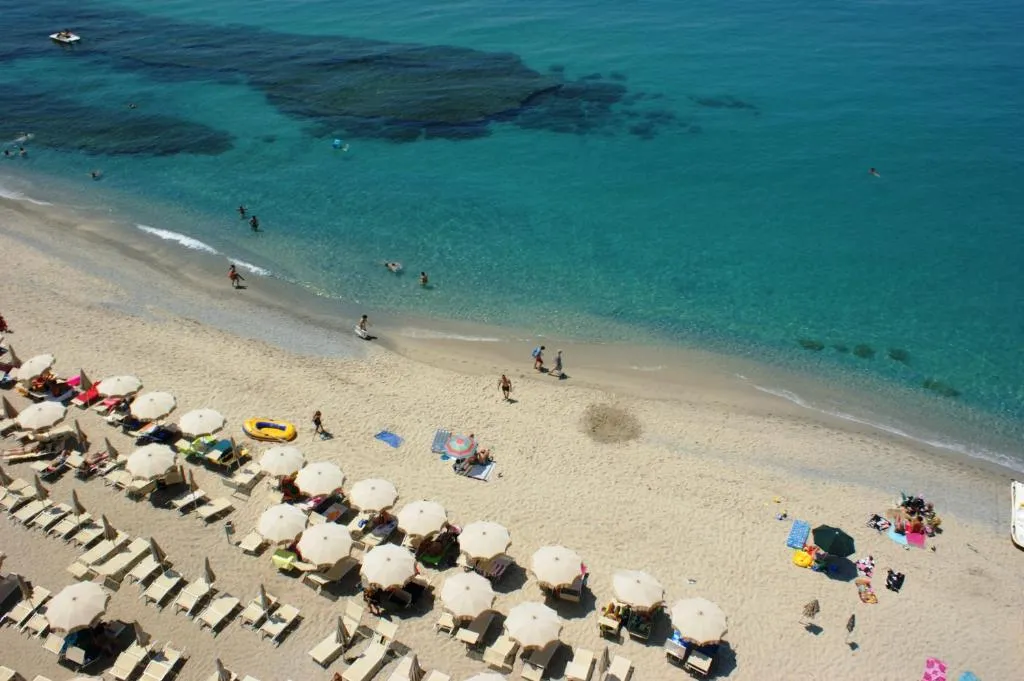 Vista dall'alto della spiaggia con ombrelloni bianchi e bagnanti nel mare azzurro trasparente