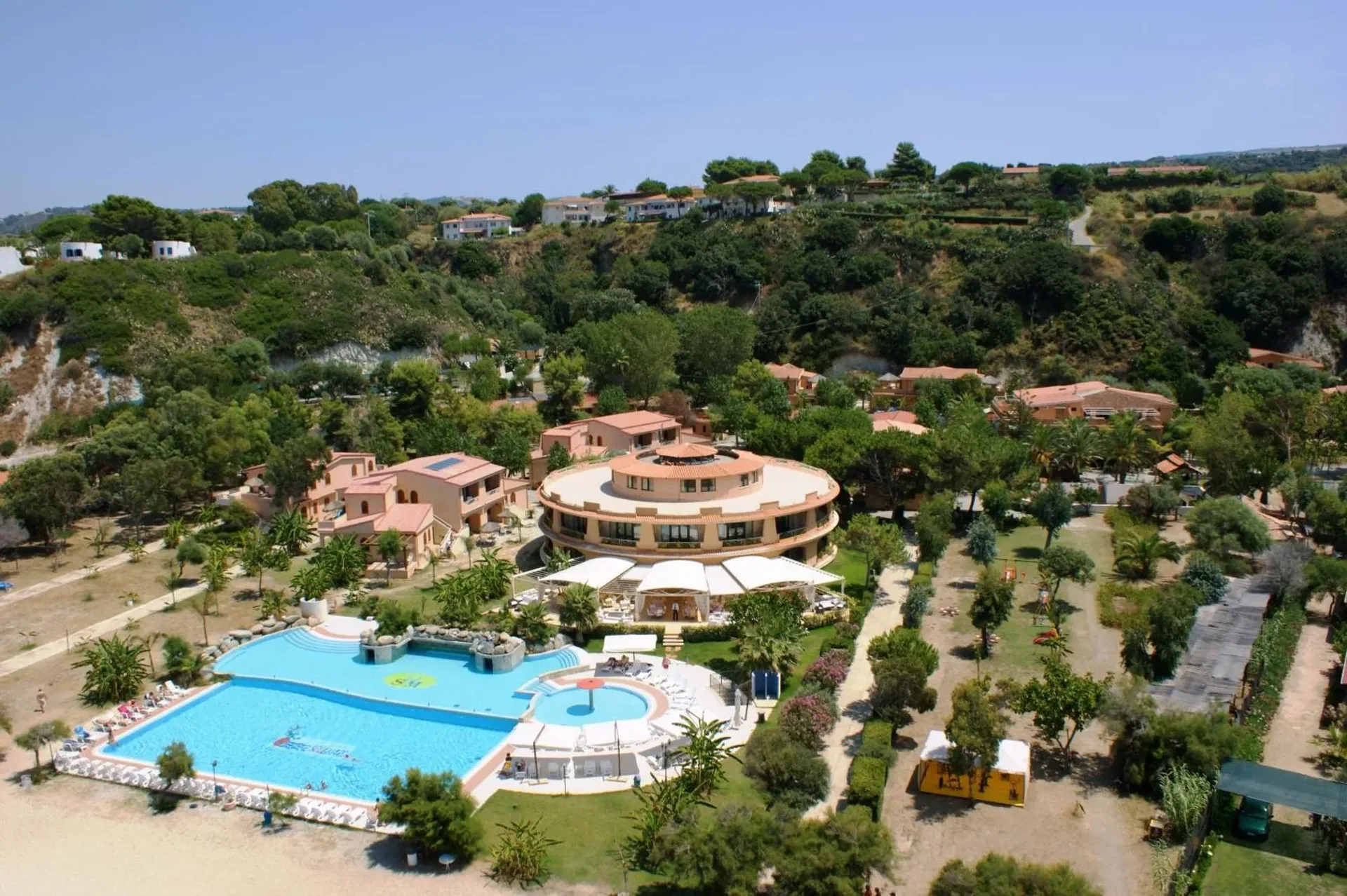 Veduta aerea del resort immerso nel verde con grande piscina ed edificio circolare