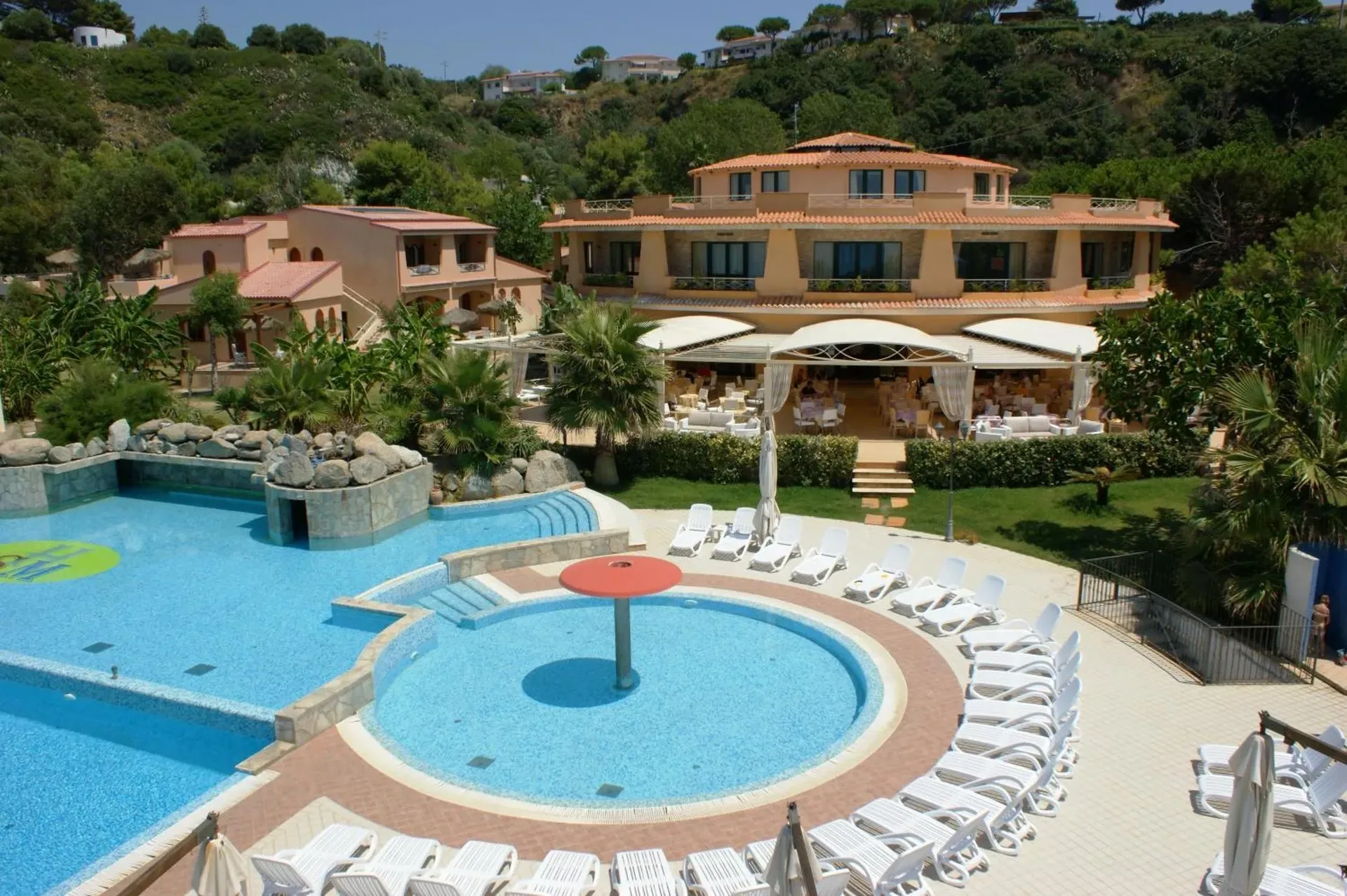 Vista del resort con piscina, vasca rotonda, lettini e edificio principale immerso nel verde