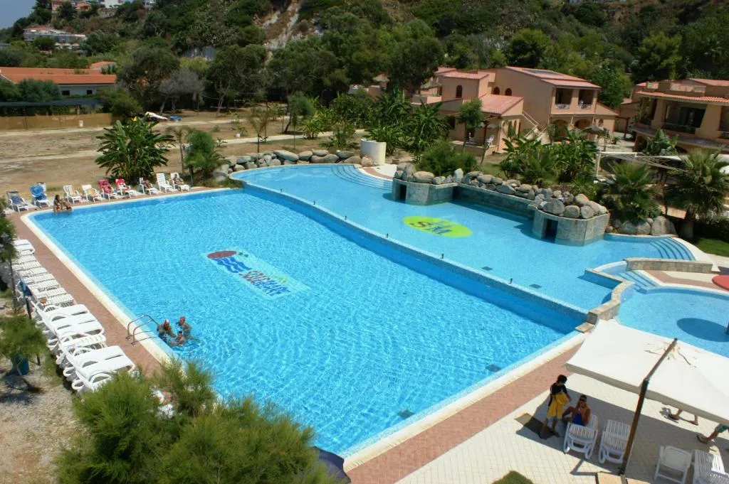 Veduta dall'alto della piscina del resort con lettini bianchi e colline verdi sullo sfondo