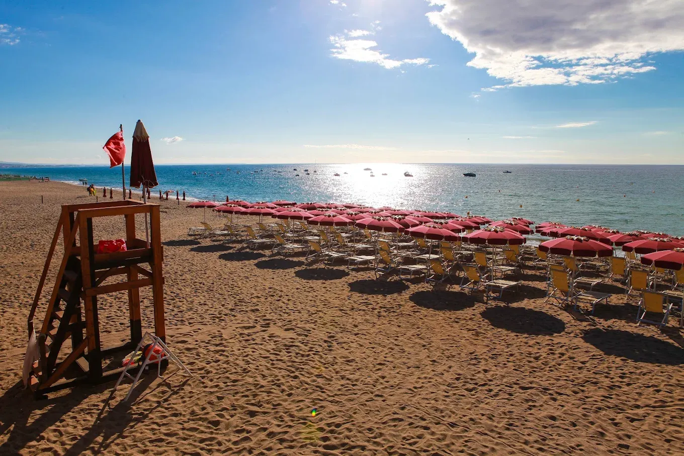 Spiaggia al tramonto con ombrelloni rossi e torretta di salvataggio