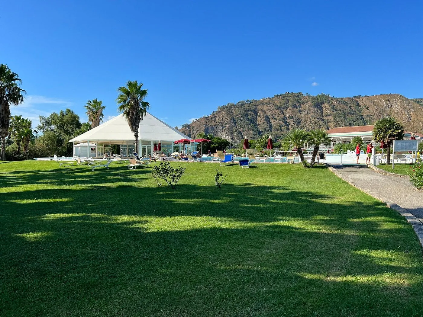 Prato verde del resort con gazebo e piscina sullo sfondo montano