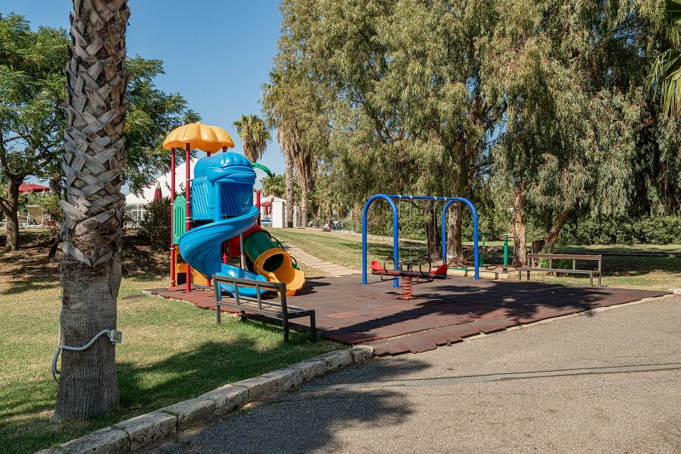 Area giochi per bambini con scivolo colorato e altalene tra le palme