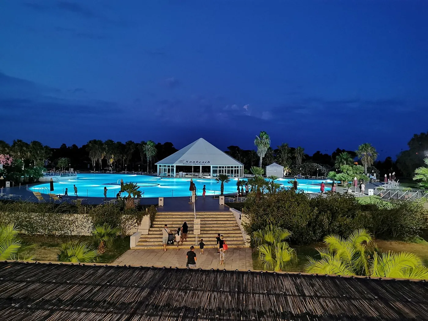 Vista serale della grande piscina illuminata con ospiti e gazebo