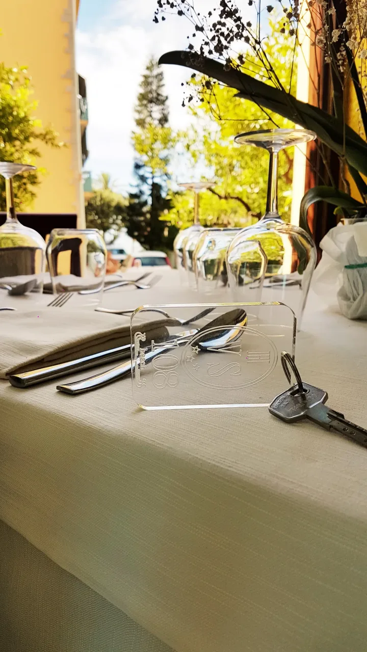 Tavolo apparecchiato all'aperto con bicchieri capovolti e chiave della camera dell'hotel