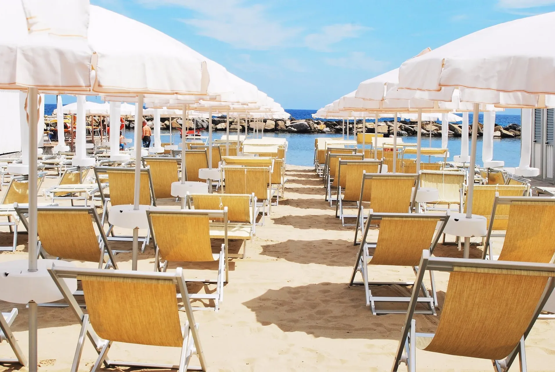 Spiaggia con sdraio gialle e ombrelloni bianchi affacciati sul mare e scogliera