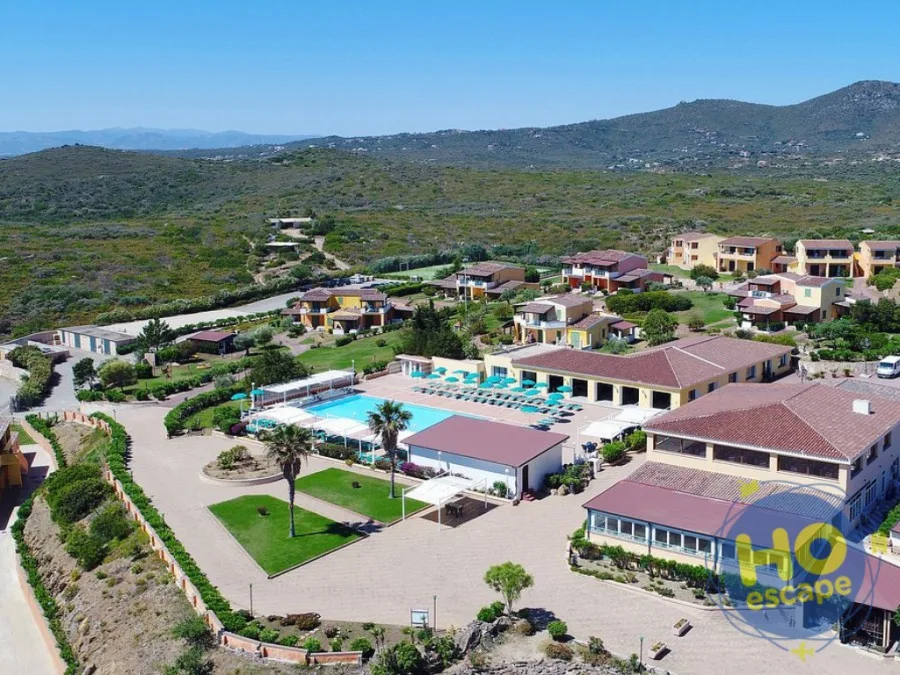 Veduta aerea del resort con piscina centrale, ville colorate e colline circostanti