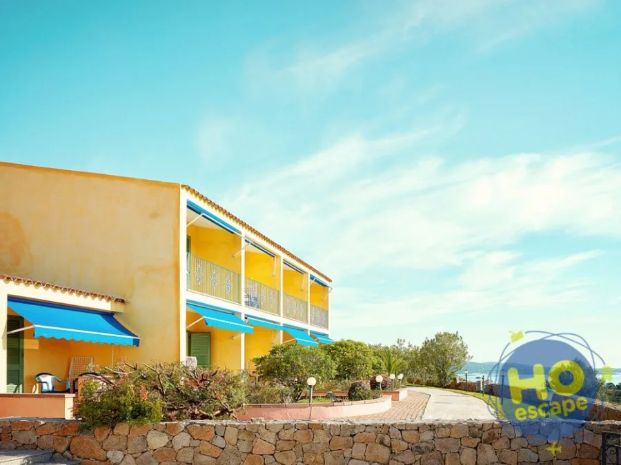 Edificio dell'hotel in giallo con tende blu e vista sul mare circondato da vegetazione