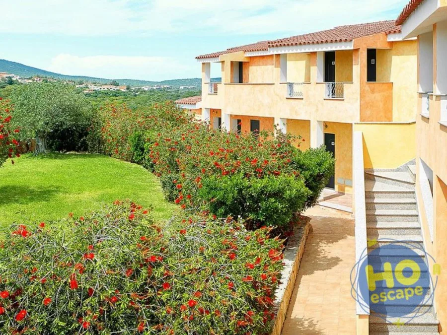 Edificio dell'hotel in giallo con giardino fiorito e siepi rosse circondato da colline