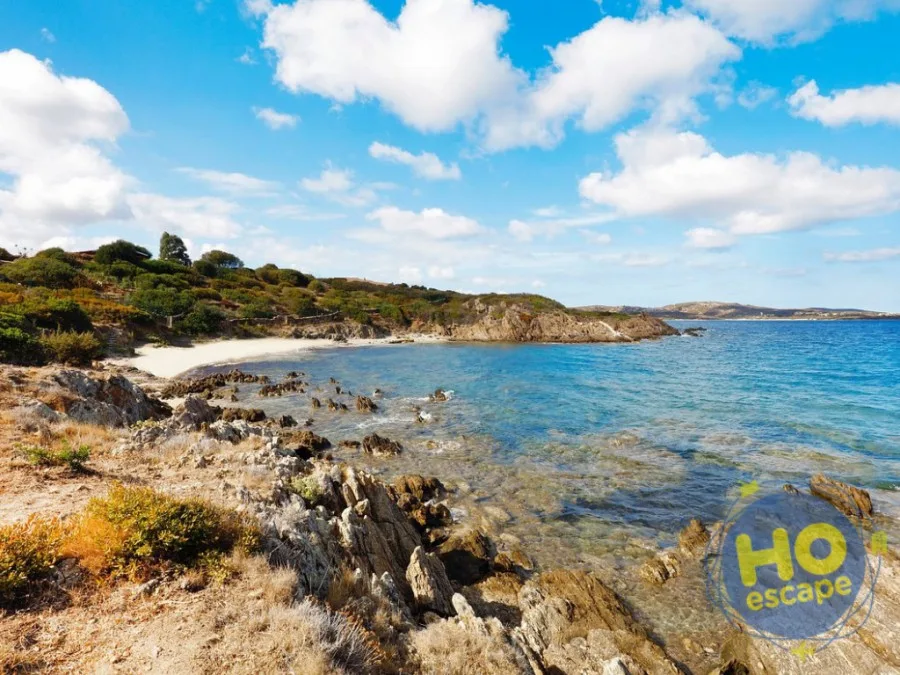 Spiaggia con sabbia chiara, mare cristallino e costa rocciosa con vegetazione