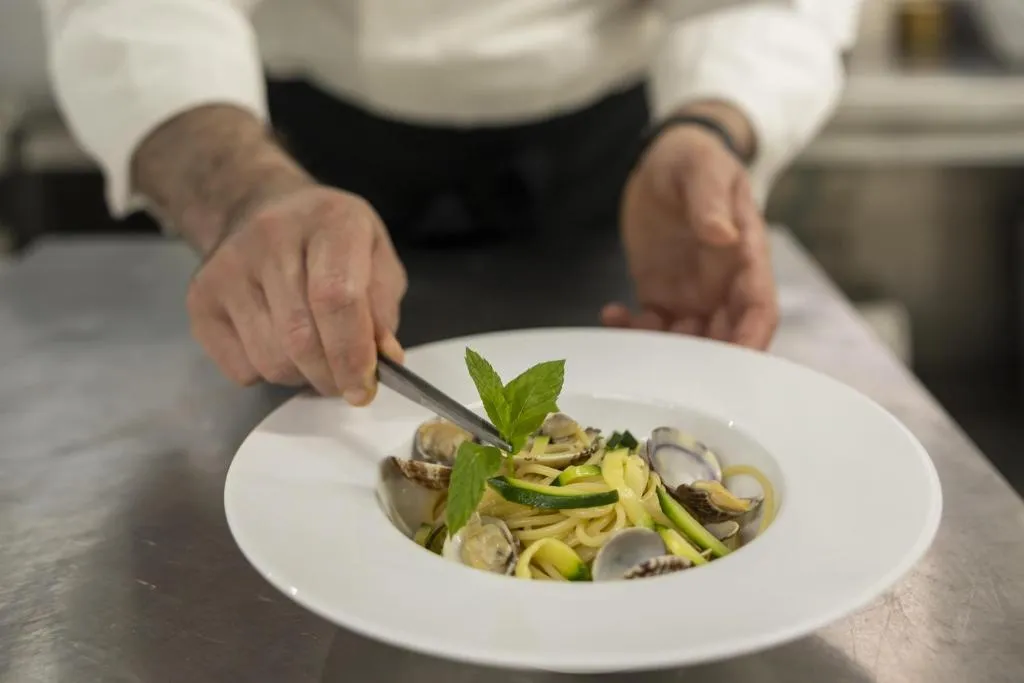Chef che impiatta spaghetti alle vongole con zucchine e menta
