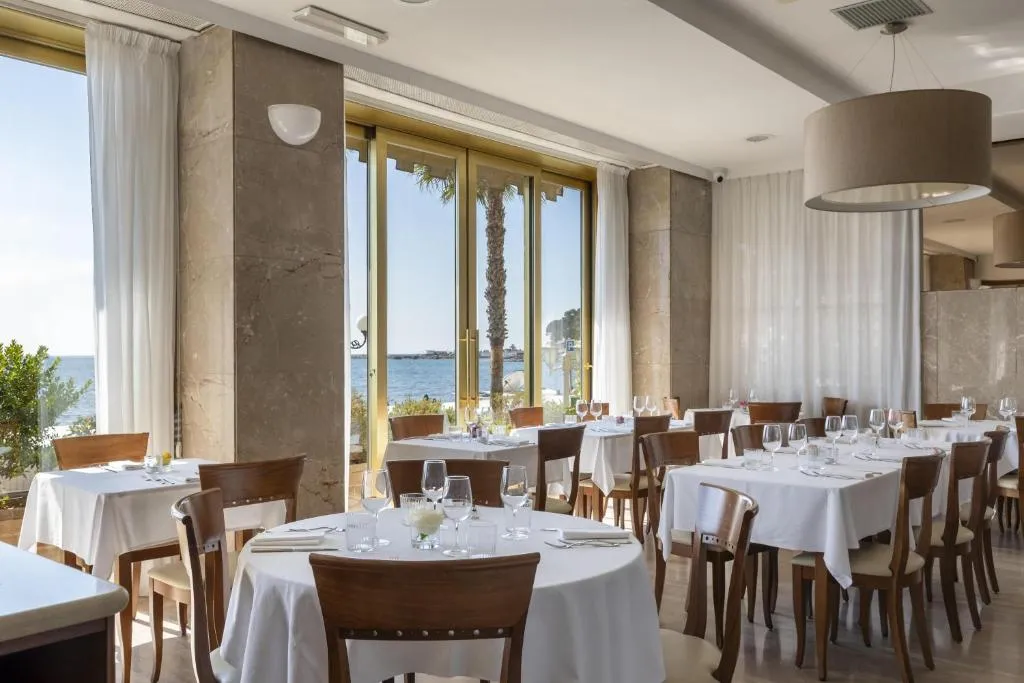 Sala ristorante elegante con tavoli rotondi e quadrati e vetrate affacciate sul mare