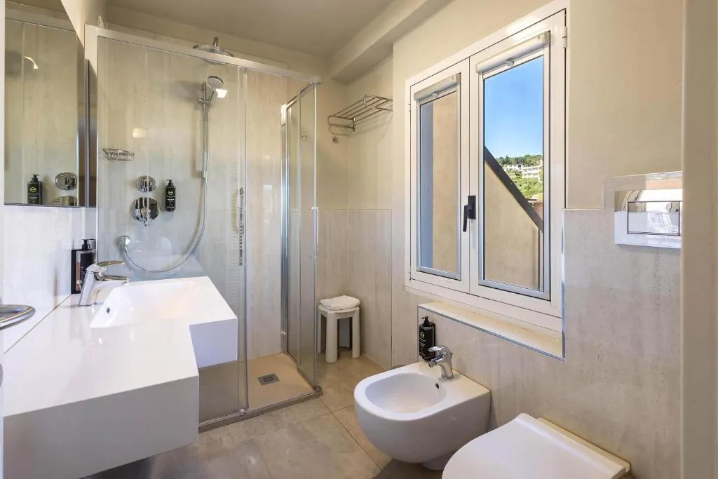 Bagno luminoso con doccia, lavabo, bidet e finestra con vista sulle colline