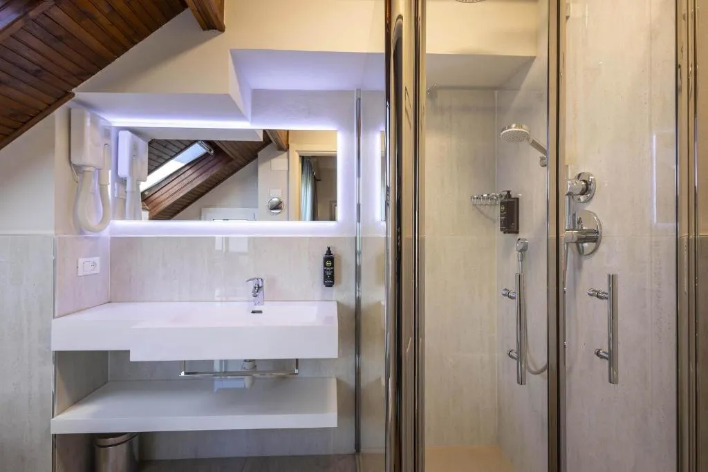 Bagno mansardato con doccia, lavabo bianco e soffitto in legno