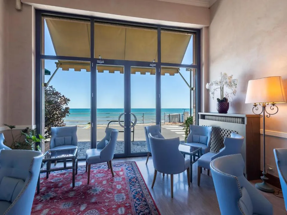 Salotto con poltrone azzurre, tappeto e grandi vetrate con vista sul mare
