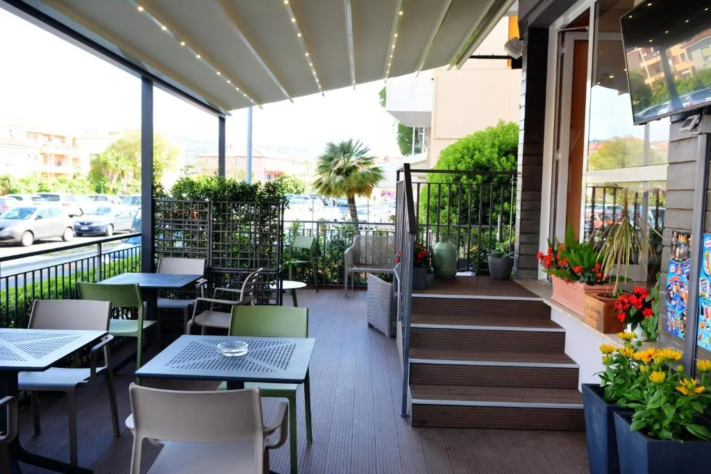 Terrazza esterna del bar con tavoli verdi, sedie e fiori colorati