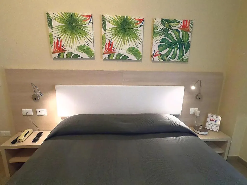 Testata del letto matrimoniale con tre quadri a tema tropicale e luci di lettura