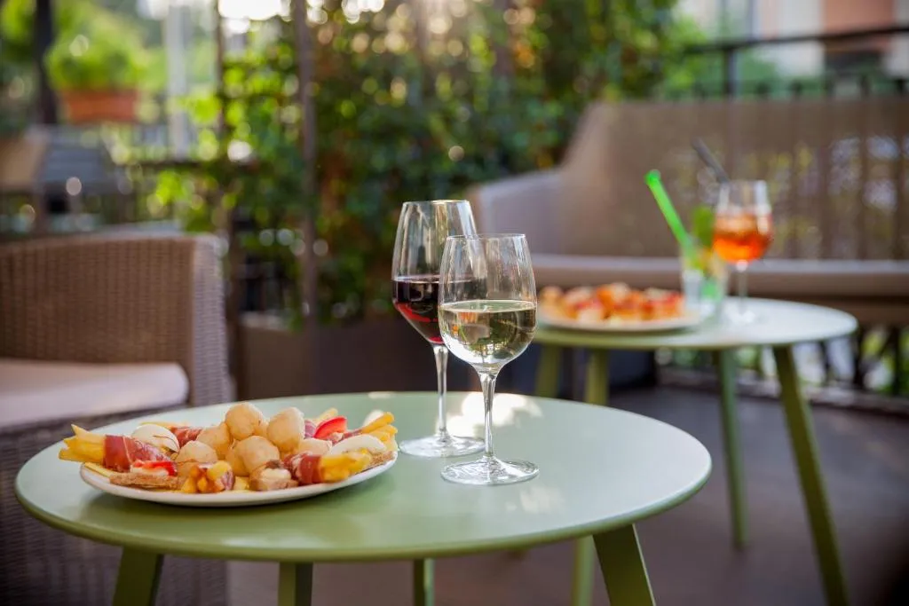Aperitivo in terrazza con calici di vino e piatto di stuzzichini su tavolino verde
