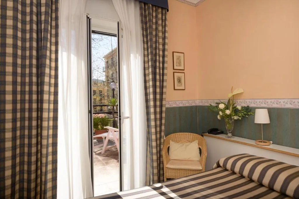 Dettaglio camera con porta finestra sul balcone, poltrona in vimini e fiori