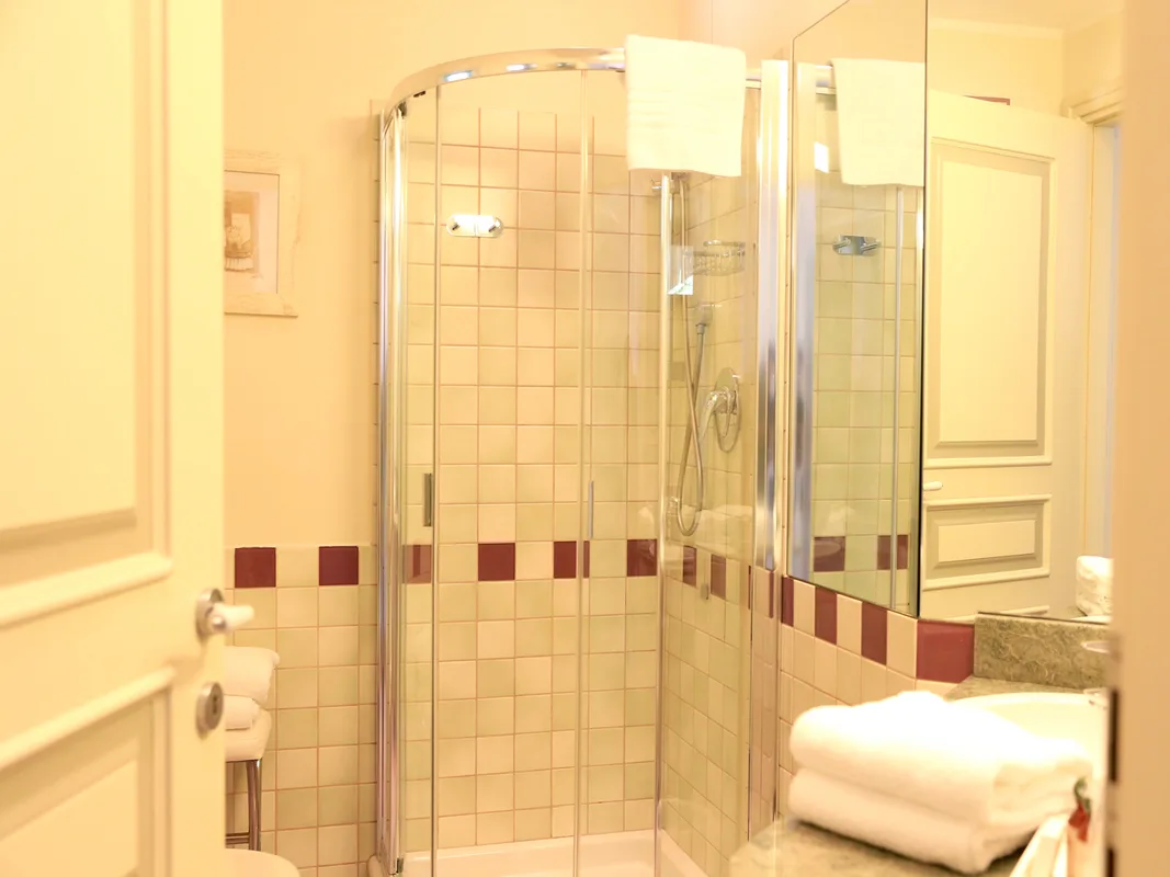 Bagno con doccia angolare in vetro, piastrelle chiare e asciugamani bianchi