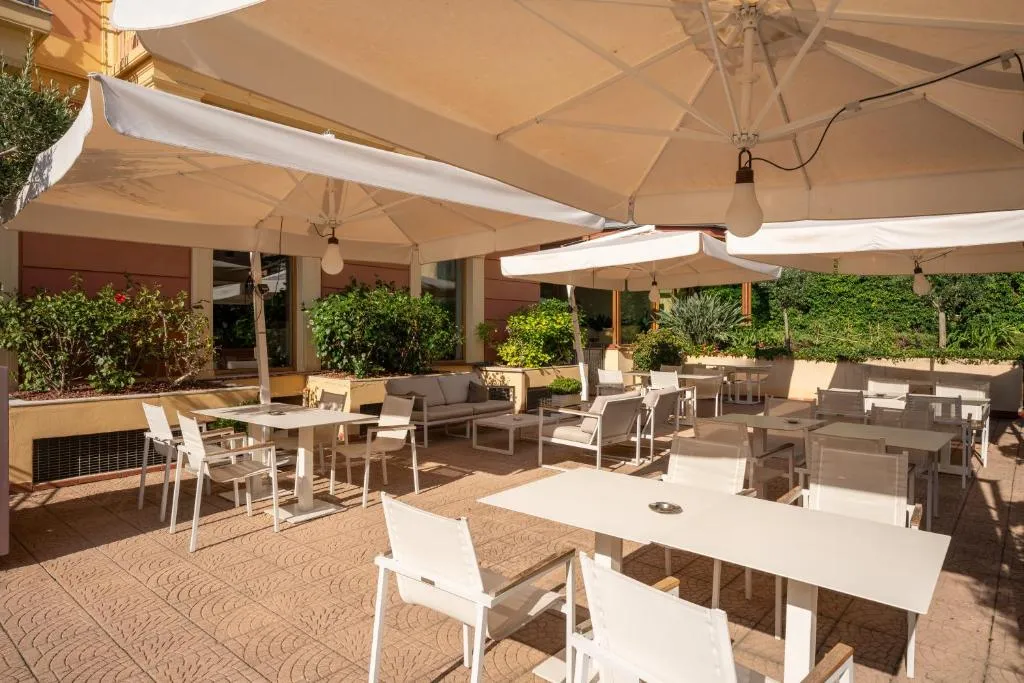 Terrazza esterna con tavoli, sedie bianche e ampi ombrelloni circondata da piante