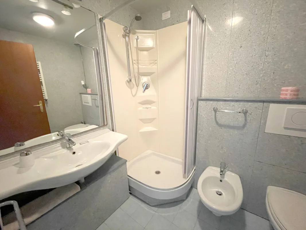 Bagno con doccia angolare, lavabo, bidet e pareti grigie