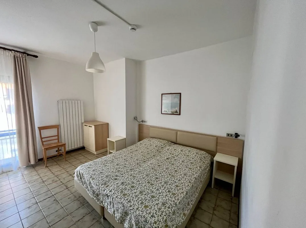 Camera da letto matrimoniale con pavimento in piastrelle e finestra con tenda