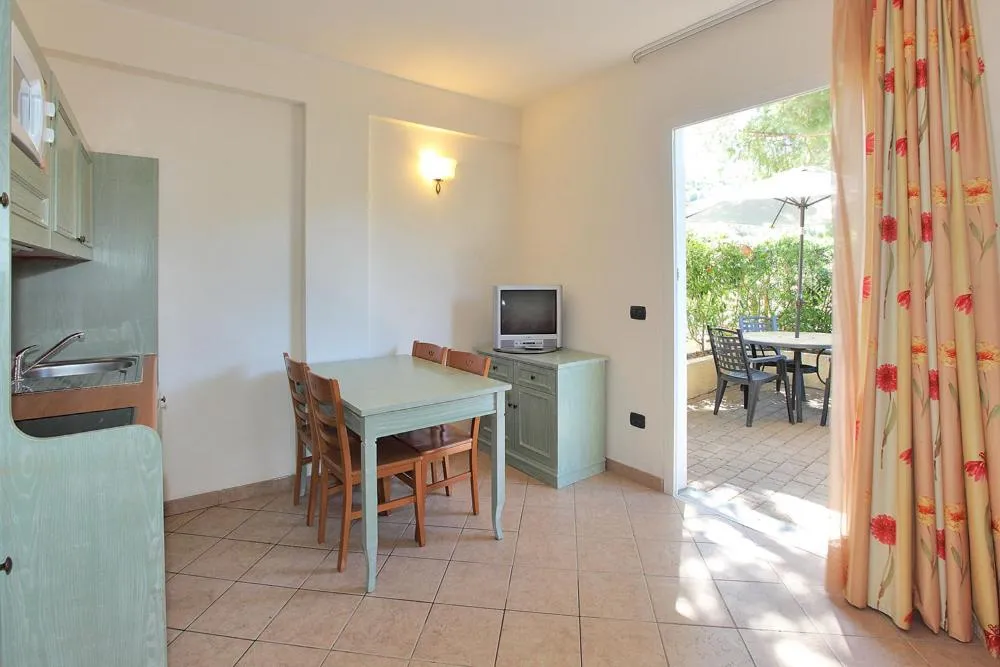 Soggiorno con angolo cucina verde, tavolo, TV e uscita verso la terrazza esterna