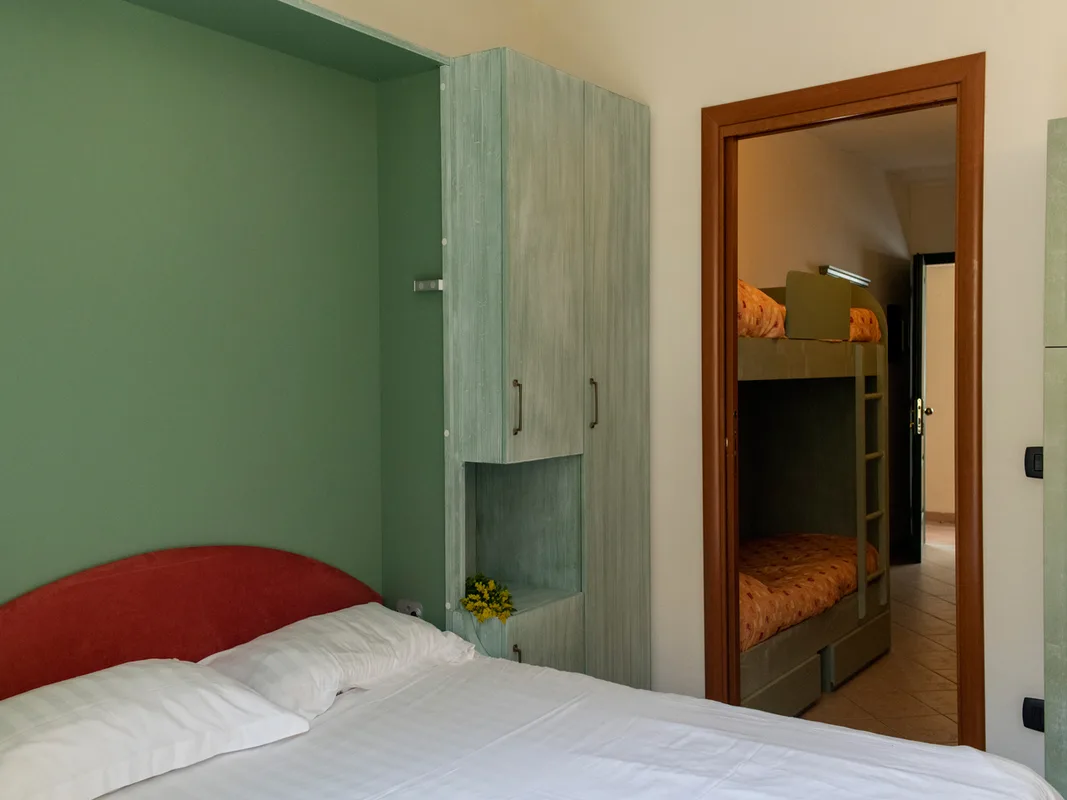 Camera con letto matrimoniale, parete verde, armadio e stanza adiacente con letto a castello