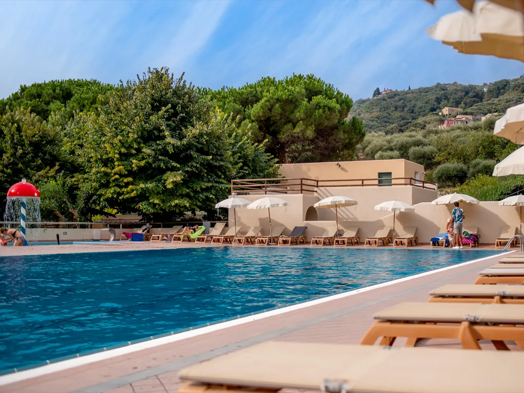 Piscina con lettini di legno, ombrelloni bianchi e vegetazione lussureggiante