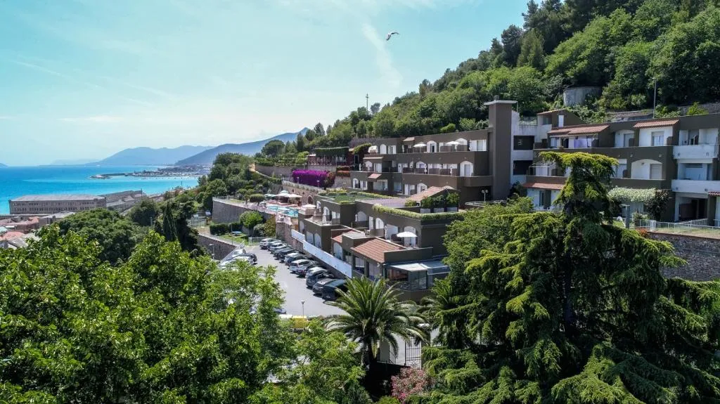 Veduta esterna dell'hotel sulla collina circondato da vegetazione con vista sul mare e sul porto