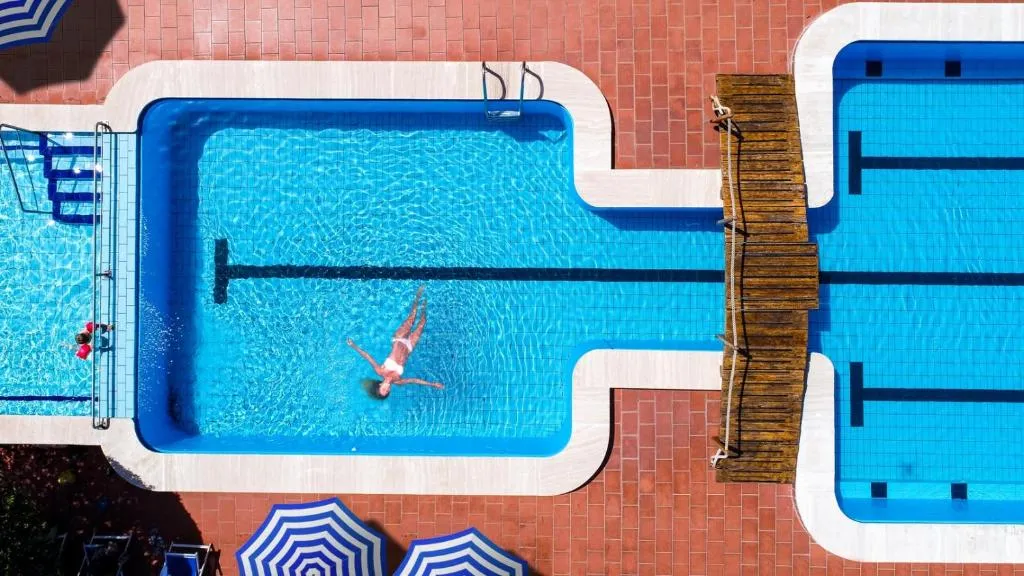 Vista dall'alto della piscina con persona che nuota e ombrelloni a righe blu